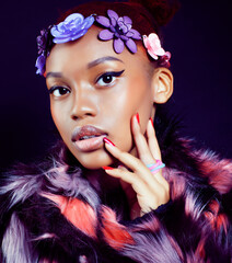 young pretty african american woman in spotted fur coat and flowers on head smiling on black background, fashion people concept