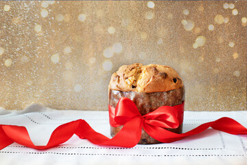 Traditional italian panettone tied with red silk ribbon on golden background with golden bokeh