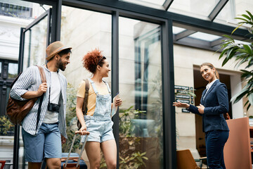 Happy receptionist greets tourist couple at hotel entrance.