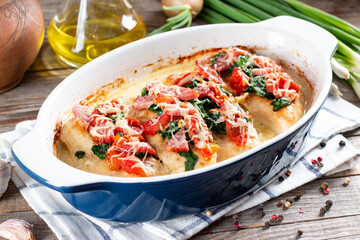 Main course baked chicken with sun-dried tomatoes and spinach in cheese sauce close-up in a pan on the table. Horizontal