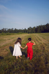 friend a boy in red clothes and a girl in a white dress walk through mown field at sunset in summer