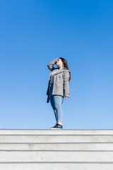 young hispanic latin woman at the top of the stairs successful. blue sky background. vertical photo with copy space
