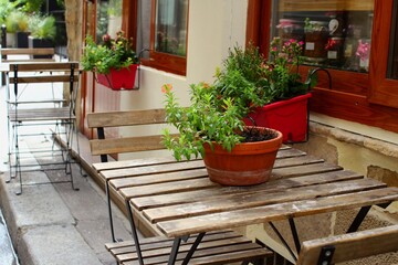 Fototapeta na wymiar Beautiful interior of Paris cafe with summer terrace and tables with house plants in the European street, French lifestyle in Europe with authentic stylish design. Empty bistro with holiday ambiance.
