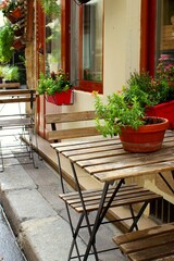 Fototapeta na wymiar Beautiful interior of Paris cafe with summer terrace and tables with house plants in the European street, French lifestyle in Europe with authentic stylish design. Empty bistro with holiday ambiance.
