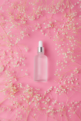 Cosmetic bottle with floral frame on pink background. Flat lay.