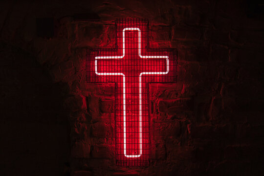 Glowing red neon cross hangs on the wall behind the bars in the dark