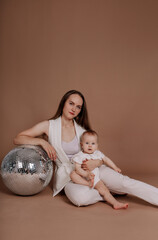 beautiful mother and daughter baby sit with a disco ball on a beige background with a place for text
