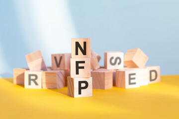 wooden cubes with letters NFP arranged in a vertical pyramid, yellow background