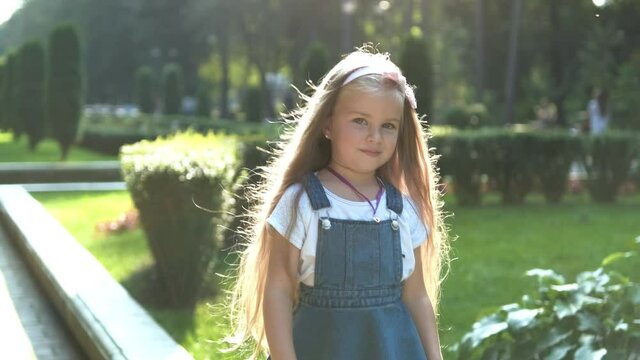 Little pretty child girl with long hair walking outdoors in green summer park on a sunny day.