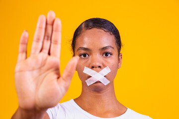 black woman on yellow background with her mouth closed in silence. Concept of prejudice, abuse and...