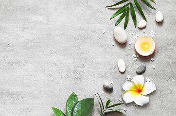 Fototapeta na wymiar Spa concept on stone background, palm leaves, flower plumeria, candle and zen, grey stones, top view.