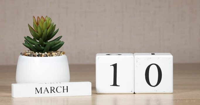Wooden calendar with an important event for march 10, a woman's hand sets the date on the calendar. Spring season.