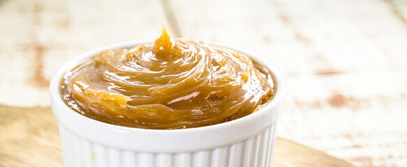 pot of dulce de leche or homemade caramel on rustic wooden background, typical Brazilian sweet