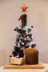 Panettone slice with Christmas tree
and blurry lights flashing in the background. Panettone concept. Christmas concept.