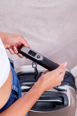 Vertical shot of a woman weighing her luggage by a digital luggage scale