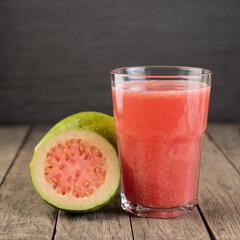 Red guava juice in a glass with  fruits over wooden table