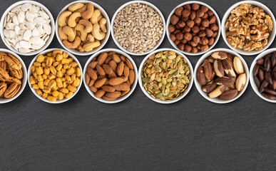 Assorted nuts and seeds in bowls over stone background with copy space