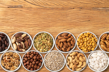 Assorted nuts and seeds in bowls over wooden table with copy space