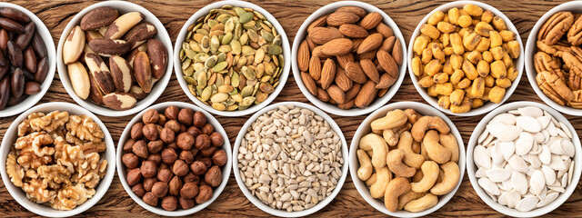 Assorted nuts and seeds in bowls over wooden table, panoramic format