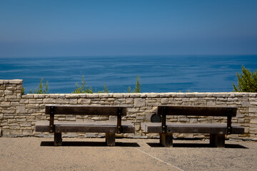 2 empty long wooden benches on the coast overlooking the blue ocean and summer sky