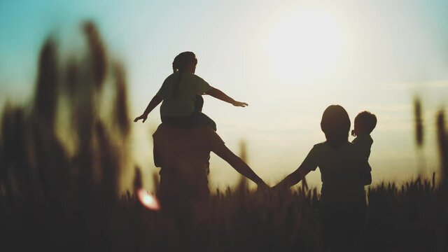 happy family in the agricultural park. silhouette of a friendly family of farmers walking in a wheat field. sunset agriculture kid dream concept silhouette. family walking in the wheat field in park