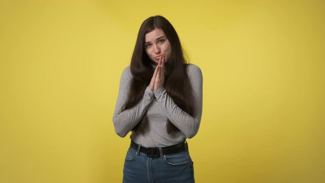 Please, bagging you. Worried slender woman in gray shirt begging you to do something. Lady pray isolated on yellow color wall background