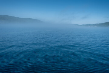 Obraz premium Lake Baikal close to village Port Baikal, Russia. Sunny day view of the high shore and clear lake water with fog