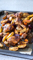 Grilled organic vegetables, potatoes, onions, beetroot, carrots, radishes with chicken legs on a baking sheet baked with herbs and spices. Top view.