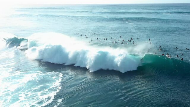 Aerial Panning Over A Group Of Surfers Paddling And Surfing Giant Crashing Waves With Bright Sunlight And White Foaming Surf - Oahu, Hawaii