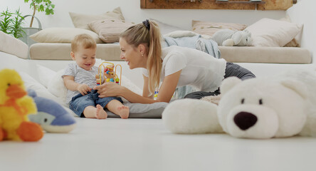 Happy and smiling mom with child baby playing with wooden toys and plush stuffed animals, at home...
