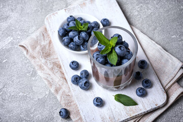 Chocolate pudding with blueberry and mint in glass on white wooden board