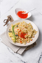 Farfalle pasta with red caviar in white bowl and cheese, green onion, pumpkin seeds, nuts