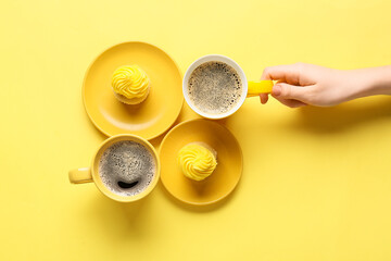 Female hand and cups of coffee with cupcakes on color background