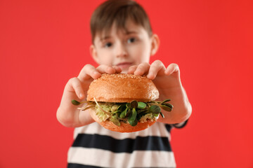 Little boy with tasty vegan burger on color background, closeup