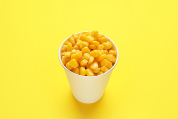 Paper cup of corn kernels on color background