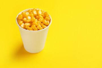 Paper cup of corn kernels on color background