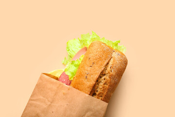 Bag with tasty ciabatta sandwich on color background