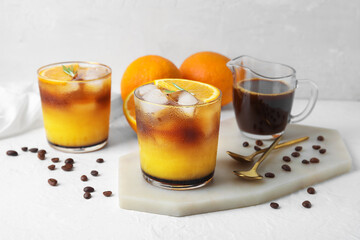 Glasses of tasty coffee with orange juice on light background