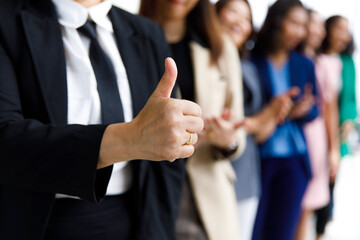 Unrecognizable unidentified female officer staff in business suit show thumb up while others standing ovation side by side applauding hands showing warm greeting celebration in blurred background