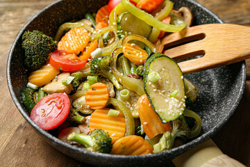 Frying pan with different vegetables on wooden background, closeup