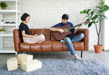 Young lovers spend time together on holidays in the living room. Asian man with headphones playing...