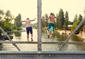 Daring young boys jumping off a bridge into the river. View from behind. Concept photo of being adventurous, fearless and brave, diving right into the water. 