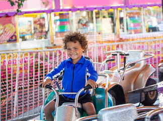 Cute mixed race little boy enjoying a ride on a fun carnival carousel ride. A happy boy Smiling and...