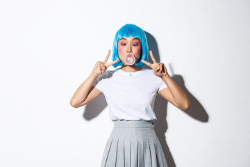 Silly asian girl in blue wig, dressed-up as anime character with colorful makeup, showing peace...