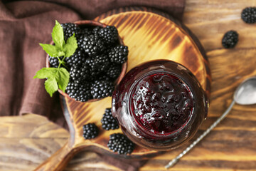 Jar of tasty blackberry jam and berries on wooden background