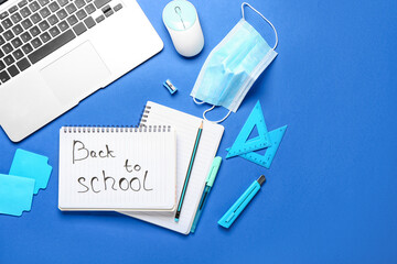 Notebook with text BACK TO SCHOOL, set of stationery, laptop and medical mask on color background