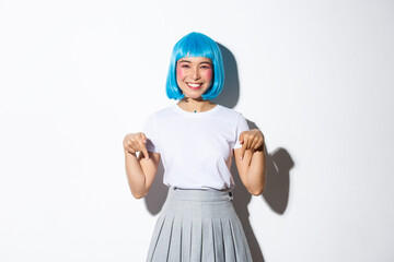 Cheerful asian woman in anime style outfit, wearing blue wig and smiling happy, pointing fingers...