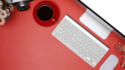 Modern workspace with computer, coffee cup and camera on red background.