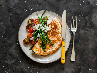Oatmeal pancake without flour with asparagus, feta and cherry tomatoes - a delicious diet breakfast on a dark background, top view