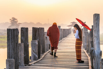 Burmese girls pay homage to the monks passing by on the bridge. Woman wearing traditional clothes...